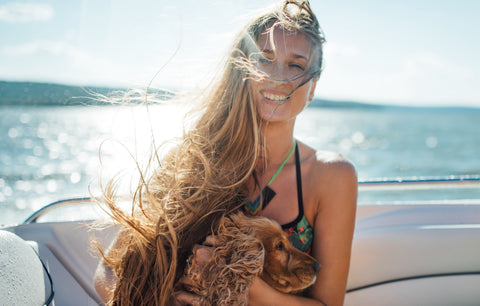 Eine Frau sitzt mit wehenden Haaren auf einem Boot und hält einen Hund im Arm