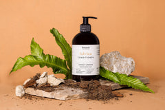 Eine Flasche Botanic Switzerland Conditioner steht auf einer Steinplatte, umgeben von Steinen, Blättern und Erde