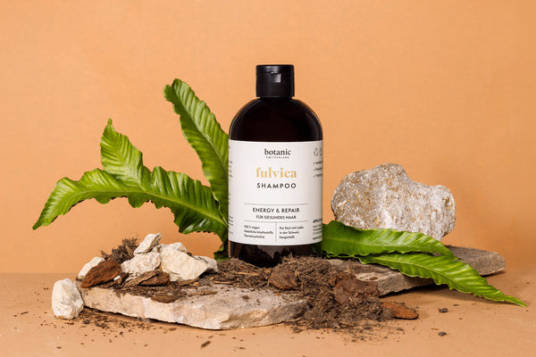 Botanic Switzerland Shampoo steht auf einer Steinplatte, im Hintergrund Blätter, im Vordergrund Erde